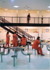 several inmates sit at tables in their pod while a corrections officer walks the second floor