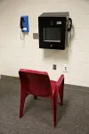 A chair in front of a video visitation station attached to a white cinderblock wall