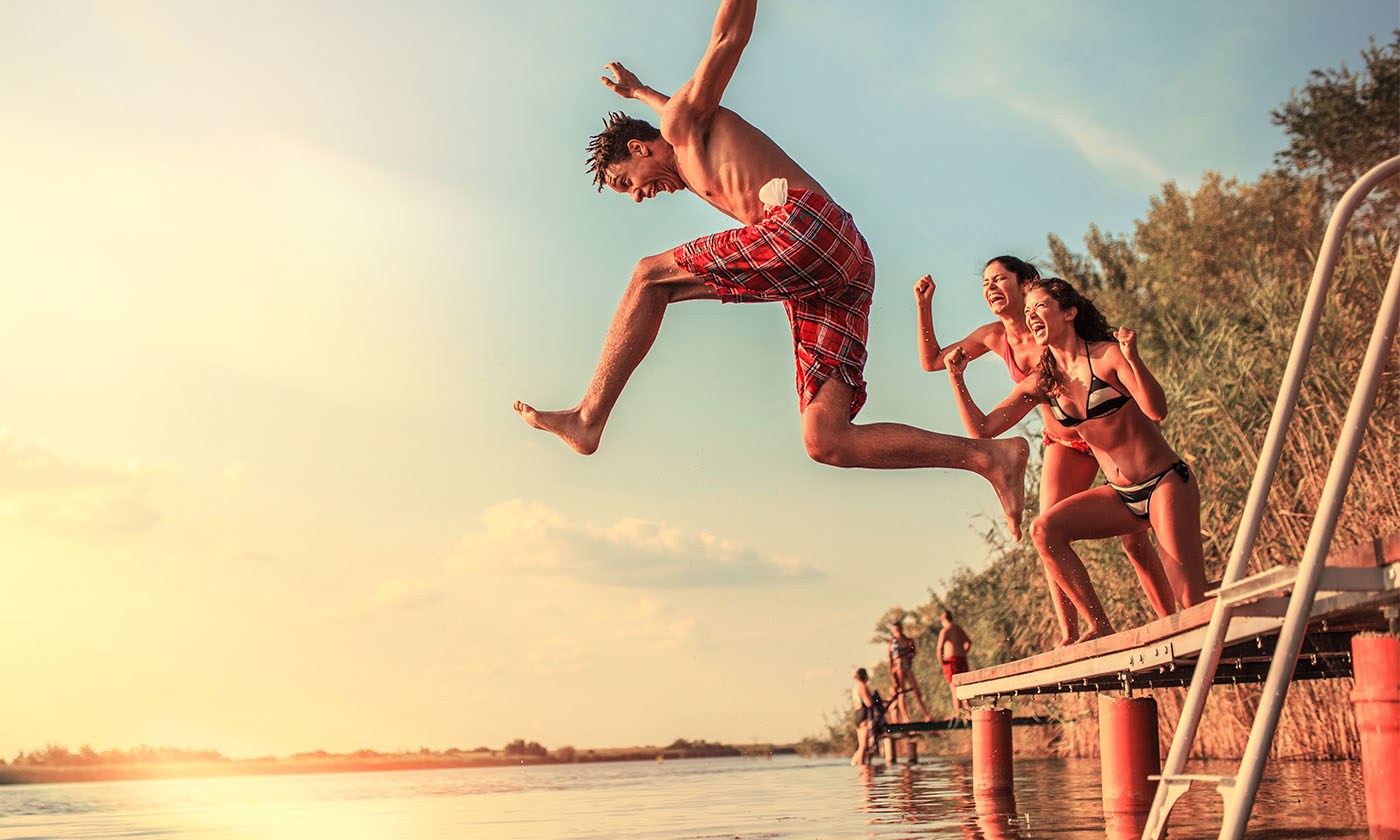 Guy in swim trunks jumping off of a dock into a lake