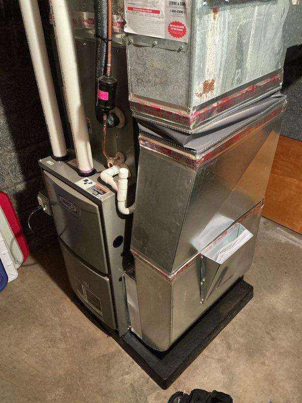 Performed annual maintenance on Lennox furnace system in basement utility area. Inspected and cleaned unit components, checked ductwork connections noting some corrosion at joints with red sealing material. Verified proper operation of condensate drain lines, valves and control interfaces with system functioning correctly as scheduled.