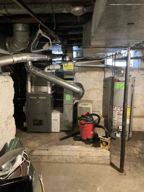 Completed comprehensive evaluation of HVAC system replacement needs for 2148 sq. ft. residence with existing Rheem furnace and 16-year-old Carrier 3.5 ton air conditioner. Inspection of basement utility area revealed new furnace installation with proper PVC venting system (purple primer marks visible at joints), while confirming the aging AC unit requires replacement. Documented current system configuration to prepare appropriate replacement options for the air conditioning component.