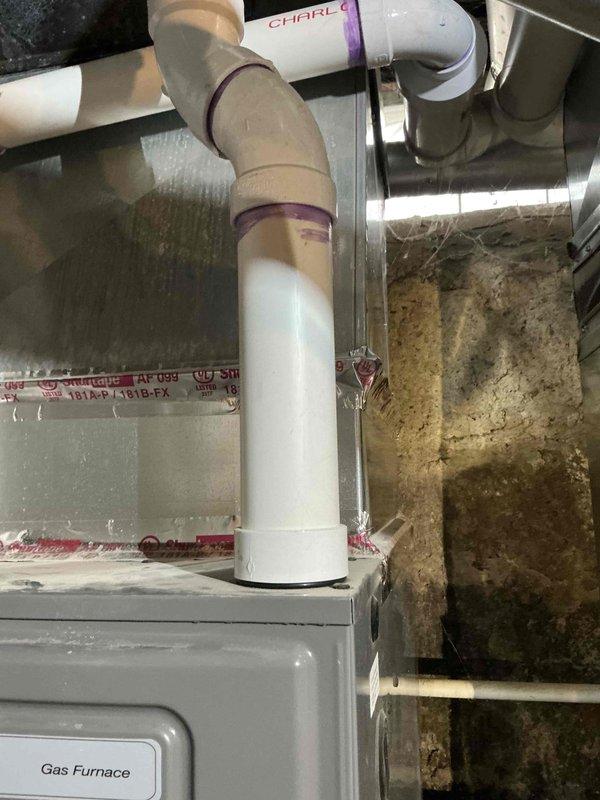 Completed comprehensive evaluation of HVAC system replacement needs for 2148 sq. ft. residence with existing Rheem furnace and 16-year-old Carrier 3.5 ton air conditioner. Inspection of basement utility area revealed new furnace installation with proper PVC venting system (purple primer marks visible at joints), while confirming the aging AC unit requires replacement. Documented current system configuration to prepare appropriate replacement options for the air conditioning component.