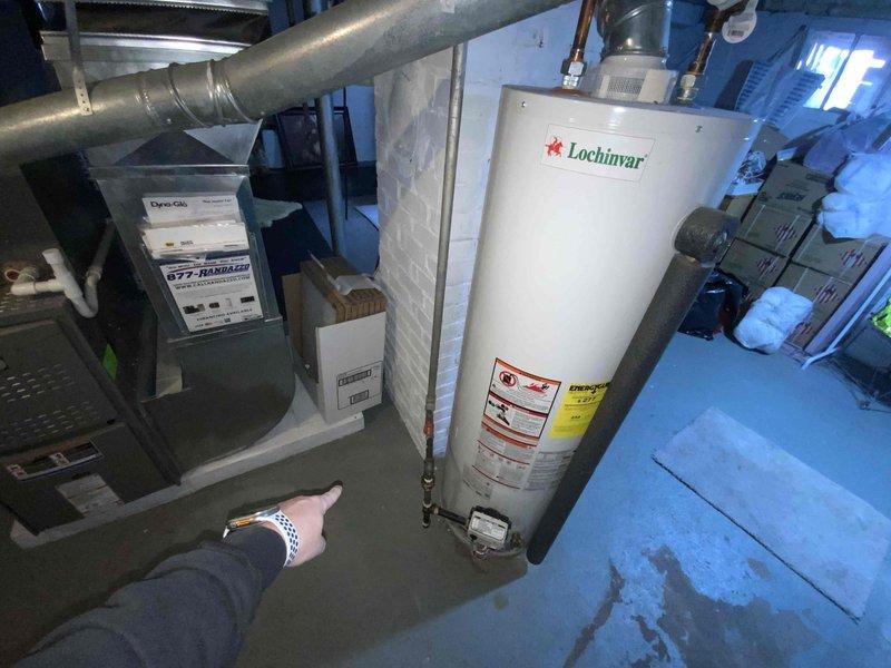 Performed diagnostic assessment on non-functioning Lochinvar water heater in utility room with associated plumbing and ventilation systems. Identified unit appears to be a commercial-grade installation with multiple connection points requiring evaluation. Documented existing configuration including PVC venting, supply lines, and proximity to Dyna-Glo furnace to prepare comprehensive replacement estimate.