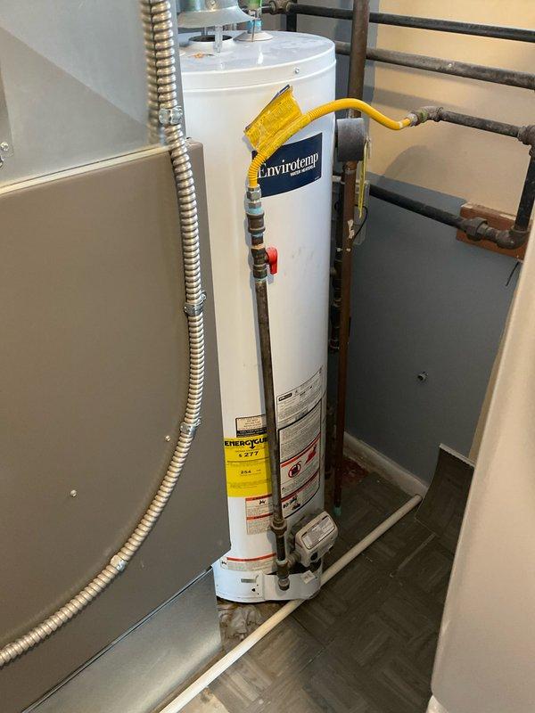 Inspected 40-gallon Envirotempo natural gas water heater that was reported leaking. Unit is installed in utility closet with proper gas line connection, copper pipe fittings, and metal vent pipe. Recommended replacement with standard tank water heater due to active leak and visible deterioration of tank integrity.