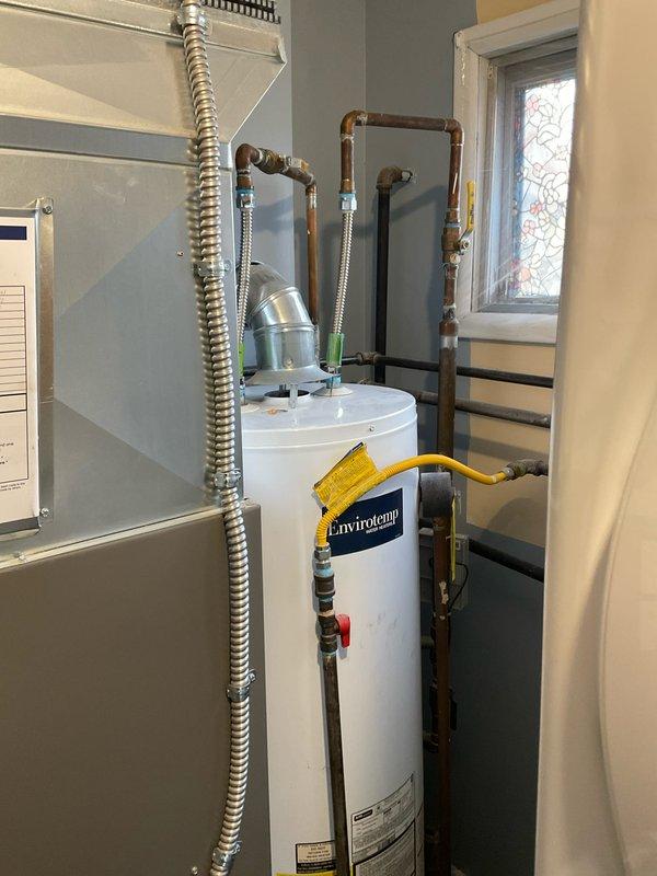 Inspected 40-gallon Envirotempo natural gas water heater that was reported leaking. Unit is installed in utility closet with proper gas line connection, copper pipe fittings, and metal vent pipe. Recommended replacement with standard tank water heater due to active leak and visible deterioration of tank integrity.
