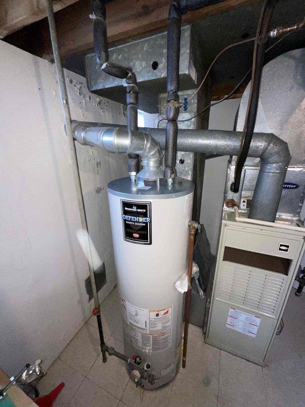 Conducted assessment of 30-year-old basement furnace for potential replacement. Observed significant wall deterioration with peeling paint around ductwork, suggesting possible moisture issues. System includes older galvanized ductwork connected to the furnace unit, with nearby water heater ("Defender" model) sharing the utility space.