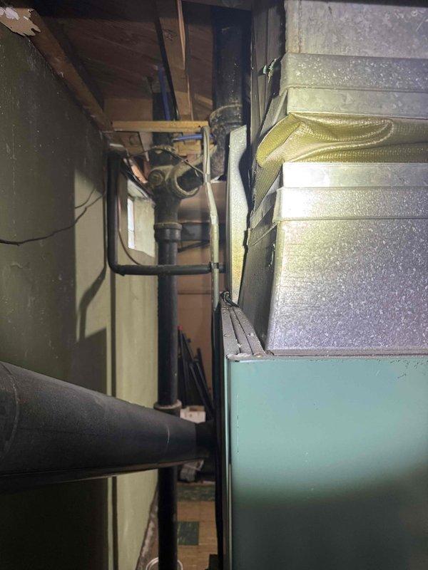 Conducted estimate for replacement of 50+ year old natural gas furnace and AC system located in basement. Current equipment is still operational but aged well beyond expected service life. Observed existing ductwork with 8" connections and noted the flow direction markings. System includes teal-colored furnace housing with metal ductwork secured by yellow strapping.