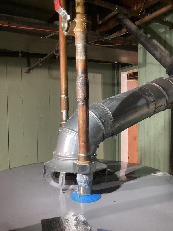 Diagnosed and repaired leaking connection point on 50+ year old tanked water heater system. Identified significant corrosion and mineral buildup at copper pipe junction, with visible oxidation staining on surrounding components. Serviced deteriorated fittings and inspected exhaust ventilation to ensure proper functionality and prevent future leakage issues.