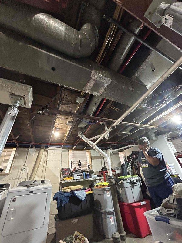 Conducted assessment for new tankless water heater installation in residence with natural draft system. Inspected basement/crawlspace area, noting existing plumbing infrastructure with accessible red and blue water lines. Evaluated current ventilation system and available utility connections to determine proper installation requirements for the requested tankless unit.