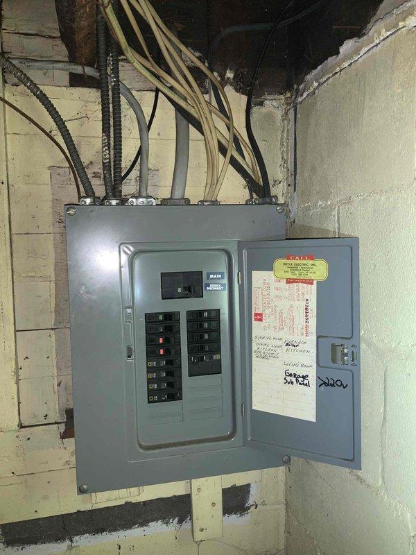 Performed comprehensive electrical inspection of residential main panel located in basement/utility area. Panel inspection revealed multiple circuit breakers with handwritten labeling including "GARAGE" and "220V" circuits. Exterior inspection identified service entrance configuration and utility connections, with documentation of all electrical distribution components via detailed photographs.