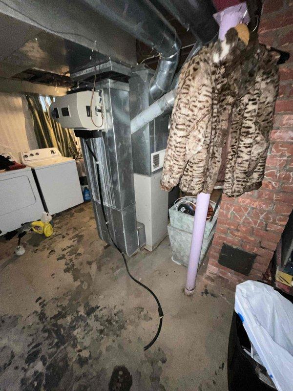 Conducted HVAC system replacement quote in basement utility area. Existing unit shows signs of age with visible duct deterioration and possible moisture issues as evidenced by floor staining. Quoted BOGO promotion for complete system replacement including furnace and associated ductwork modifications.