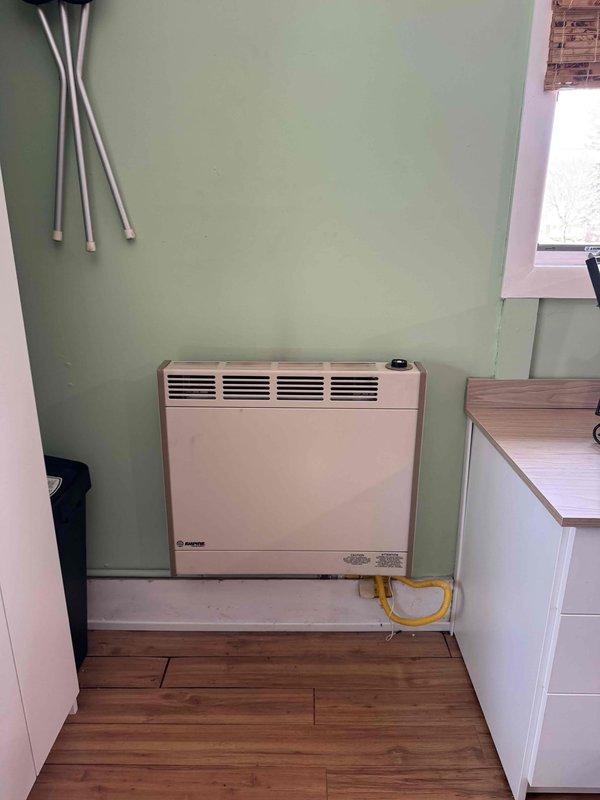 Conducted replacement estimate for 20-year-old direct vent wall furnace in residential property. Inspected existing unit mounted on mint green wall with yellow gas line connection, noting age-related wear. Documented current installation configuration for proper sizing of replacement equipment.
