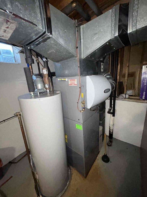 Conducted assessment of non-operational 15-year-old gas furnace and AC system located in basement. Inspection revealed aging ductwork with visible manufacturer labels and deterioration. Photographed existing installation including furnace, water heater, humidifier attachment, and galvanized sheet metal ductwork configuration for replacement quote preparation.