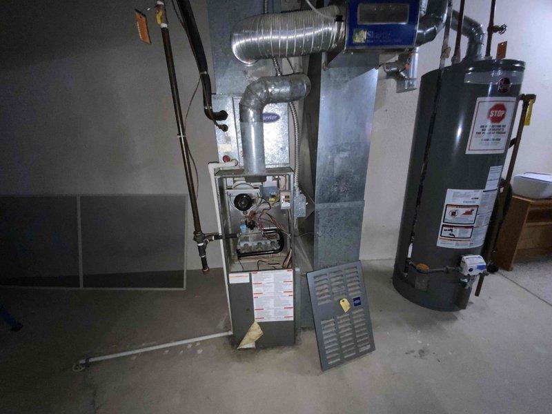 Conducted a full system estimate on an aging 10-year-old AC unit that requires immediate replacement. Inspected the existing installation which includes a furnace with exposed control board, metal ductwork with multiple connection points, and adjacent water heater system. Documented the confined installation space and current configuration to develop appropriate replacement options for the customer's right-away timeline.