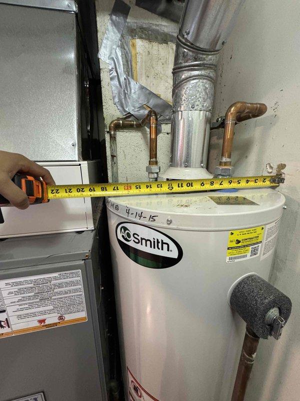 Inspected non-functional A.O. Smith water heater (installed 4-14-15) for replacement. Observed deteriorated ductwork connection and makeshift repairs with duct tape at wall penetration. Took measurements of existing tanked unit and surrounding installation constraints to prepare estimate for standard water heater replacement.
