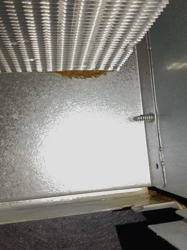 Performed routine Air Handler Maintenance inspection and identified significant mineral deposits on floor surface beneath unit, likely from condensate drainage issues. Documented substantial rust formation along heat exchanger/coil junction with housing, indicating potential moisture intrusion and ongoing corrosion that may require future remediation.