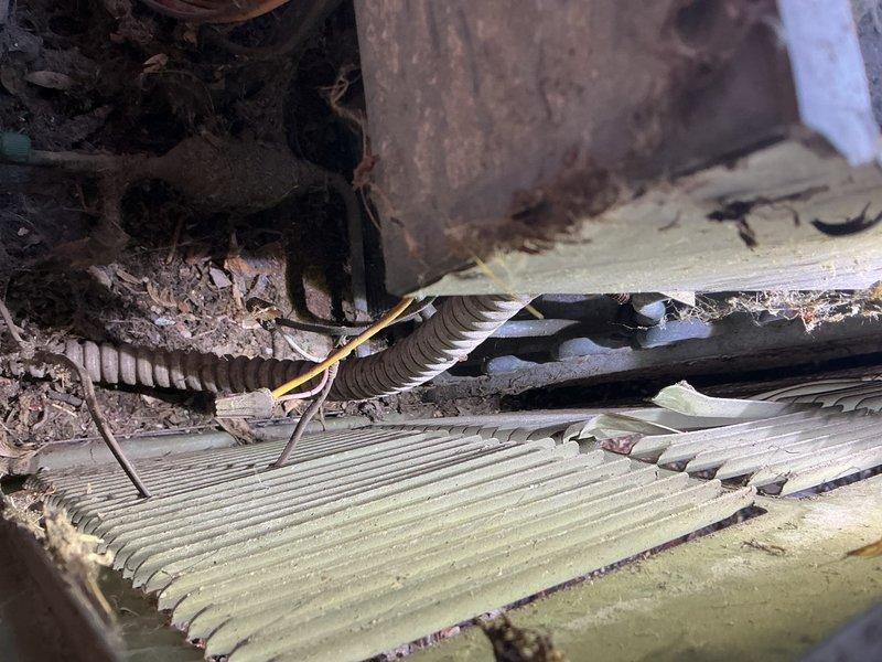 # HVAC Service - A/C Inspection Following Storm Damage

Responded to service call for air conditioning unit damaged by fallen tree branch. Upon arrival, performed comprehensive visual inspection of outdoor condensing unit to assess extent of damage. Found significant impact damage to cabinet housing with bent and missing louver sections on exterior panels. Discovered compromised cabinet integrity with visible openings exposing internal components including refrigerant lines and electrical wiring.

Inspection revealed damaged evaporator coil with bent fins and debris accumulation throughout coil surfaces. Identified corroded refrigerant line connections showing pre-existing rust deterioration, now further exposed due to cabinet damage. Found flexible ductwork displaced and insulation material protruding from damaged cabinet sections. Electrical wiring remained intact but exposed to elements through cabinet openings, presenting potential safety concern.

Noted extensive organic debris in