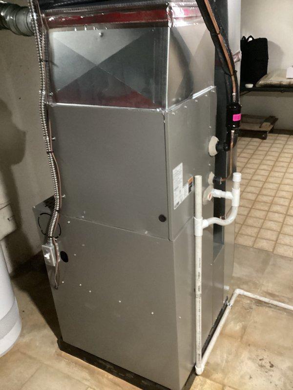 Completed warranty replacement installation of ML180 furnace unit in residential basement utility room. Installed new gray cabinet-style furnace with proper venting using white PVC piping, connected condensate drainage lines, and verified all ductwork connections including metallic flexible ducts. Ensured proper refrigerant line connections with insulation, confirmed blower compartment operation, and verified all safety labels and manufacturer specifications are visible and intact. Old unit requires return for warranty tagging processing.