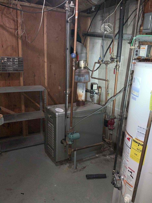 Conducted comprehensive site evaluation for complete HVAC system installation in residential property currently without existing heating or cooling equipment. Assessed basement mechanical room layout, existing utility infrastructure including water heater and plumbing systems, and evaluated available space for new furnace and air conditioning equipment placement. Documented current conditions of unfinished basement area with wood-paneled walls, exposed joists, and concrete flooring to determine optimal equipment configuration and ductwork routing. Photographed existing utility connections, electrical panel location, and structural considerations for new system installation. Provided detailed equipment recommendations and installation specifications for full heating and cooling system to be scheduled for installation at end of March.