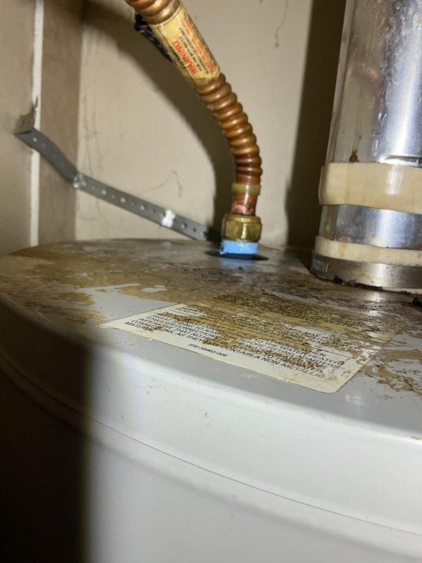 Responded to a leaking hot water tank in a 14-year-old mobile home where the tank was located in a closet and had caused water damage to surrounding carpet. Upon inspection, found a severely corroded 14-year-old tanked water heater with extensive rust staining on the top surface and failed pilot light assembly. Assessed the unit's condition, documented the leak source from the tank body itself, and determined the water heater had reached end of service life due to age and internal tank failure. Relit the pilot light temporarily and provided the homeowner with options for water heater replacement given the extent of corrosion and active tank leak.