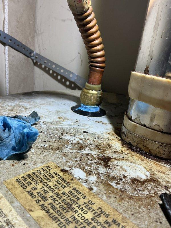 Responded to a leaking hot water tank in a 14-year-old mobile home where the tank was located in a closet and had caused water damage to surrounding carpet. Upon inspection, found a severely corroded 14-year-old tanked water heater with extensive rust staining on the top surface and failed pilot light assembly. Assessed the unit's condition, documented the leak source from the tank body itself, and determined the water heater had reached end of service life due to age and internal tank failure. Relit the pilot light temporarily and provided the homeowner with options for water heater replacement given the extent of corrosion and active tank leak.