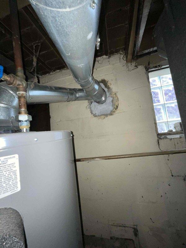 Conducted furnace replacement estimate for non-operational natural gas heating system located in basement with existing galvanized ductwork and exposed joists. Assessed current gray metal furnace unit with multiple warning labels, evaluated existing supply and return duct configuration including vertical galvanized trunk line with elbow connection, and documented utility room conditions including concrete block walls, copper gas piping with brass fittings, and available clearances for new equipment installation.