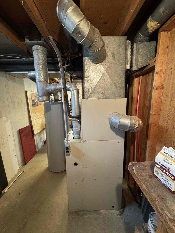 Conducted on-site assessment for air conditioning system replacement. Evaluated existing 20-year-old AC unit and associated HVAC infrastructure in basement mechanical room. Documented current equipment configuration including furnace, ductwork distribution system, and utility connections. Photographed existing installation showing white metal furnace with metallic supply ductwork, flexible and rigid duct components, and water heater placement. Assessed spatial constraints, electrical service availability, and existing duct system compatibility for new air conditioner installation. Prepared comprehensive replacement estimate for expedited installation scheduling.