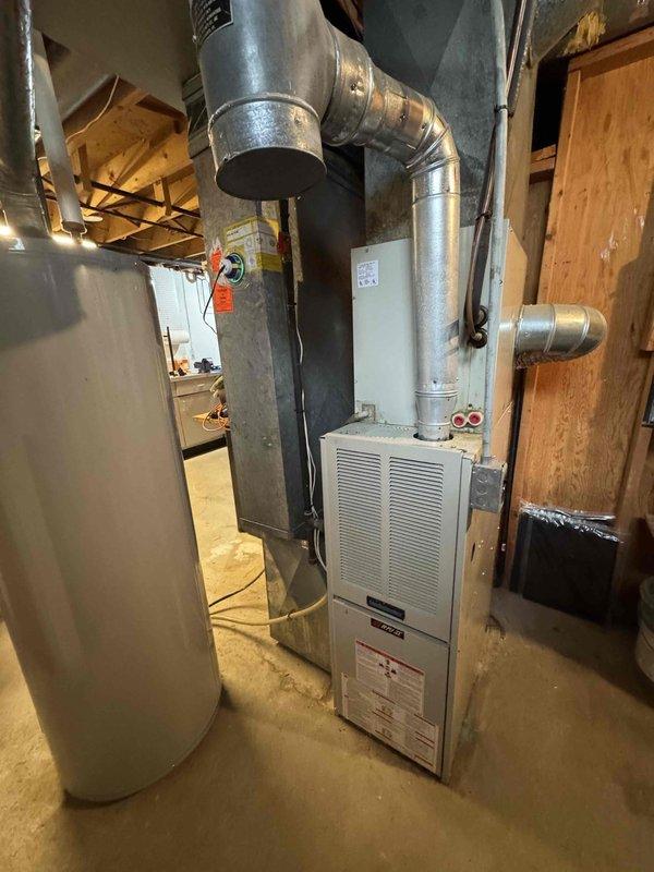 Conducted on-site assessment for air conditioning system replacement. Evaluated existing 20-year-old AC unit and associated HVAC infrastructure in basement mechanical room. Documented current equipment configuration including furnace, ductwork distribution system, and utility connections. Photographed existing installation showing white metal furnace with metallic supply ductwork, flexible and rigid duct components, and water heater placement. Assessed spatial constraints, electrical service availability, and existing duct system compatibility for new air conditioner installation. Prepared comprehensive replacement estimate for expedited installation scheduling.