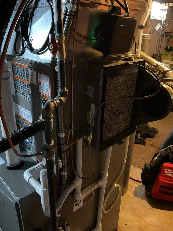 Responded to service call for filter leak on humidifier system connected to forced air furnace. Upon arrival, inspected the humidifier assembly mounted to the supply plenum and identified water leakage affecting the evaporator pad filters. Examined the white PVC water supply line connections and drain components for proper installation and secure fittings. Verified humidifier unit age at less than one year, confirming potential warranty coverage. Documented system configuration with photographs showing furnace installation, humidifier positioning, filter condition, and associated plumbing connections including copper lines and PVC drainage. Assessed evaporative pad filters for saturation and proper seating within the humidifier housing. Identified source of leak and provided recommendations for repair or warranty claim submission.