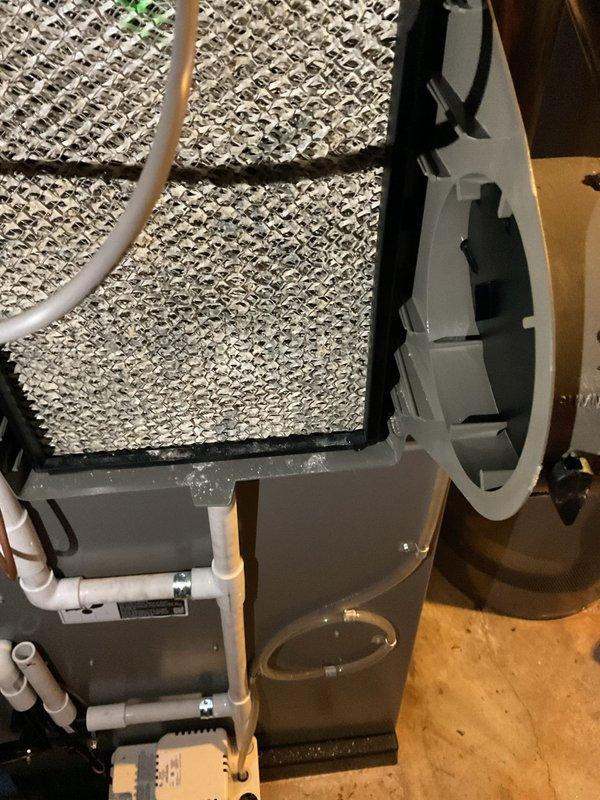 Responded to service call for filter leak on humidifier system connected to forced air furnace. Upon arrival, inspected the humidifier assembly mounted to the supply plenum and identified water leakage affecting the evaporator pad filters. Examined the white PVC water supply line connections and drain components for proper installation and secure fittings. Verified humidifier unit age at less than one year, confirming potential warranty coverage. Documented system configuration with photographs showing furnace installation, humidifier positioning, filter condition, and associated plumbing connections including copper lines and PVC drainage. Assessed evaporative pad filters for saturation and proper seating within the humidifier housing. Identified source of leak and provided recommendations for repair or warranty claim submission.