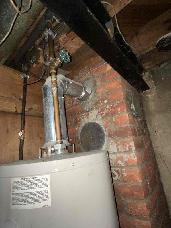 Conducted on-site assessment of residential water heater experiencing active leaking and complete heating failure. Unit is a standard atmospheric vent gas-fired water heater installed in basement utility closet with louvered door access. Inspection revealed visible water damage and staining on concrete floor beneath unit, indicating ongoing or recent leak from tank. Evaluated all plumbing connections, including copper supply lines, shut-off valves with blue handle, pressure relief valve, and flue vent system. Assessed condition of aging installation against deteriorated brick wall with exposed mortar joints. Documented compromised tank integrity and complete loss of heating function. Photographed existing installation configuration, piping layout, venting arrangement, and evidence of water damage for estimate preparation. Provided comprehensive evaluation for water heater replacement recommendation.