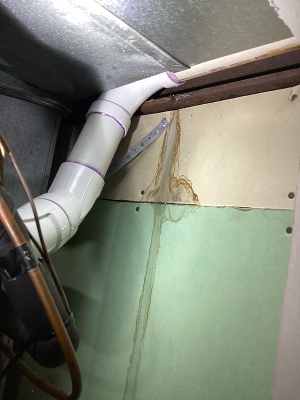 Responded to callback for water leak originating from front of heat exchanger in condo unit. Upon inspection, identified condensate drain line issue with water staining visible on interior wall surfaces and traced PVC condensate discharge line to exterior termination point. Documented conditions with interior mechanical space showing moisture damage on wall panels near HVAC equipment and exterior foundation area where condensate line exits building, confirming proper drainage pathway but requiring further evaluation of heat exchanger and condensate management system to determine root cause of leak.