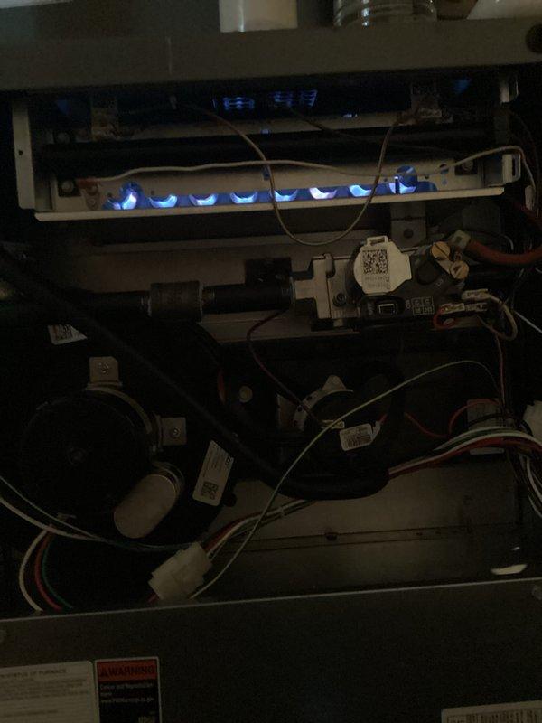 Completed annual furnace maintenance and tune-up on residential heating system. Performed comprehensive inspection of all internal components including blower motor assembly, gas valve, control board, and electrical connections. Removed upper access panel to access and evaluate burner assembly, heat exchanger, and ignition system. Verified proper gas combustion with blue flame pattern across all burner ports, indicating optimal air-to-fuel ratio. Inspected all wiring connections including ground, neutral, and control circuits for secure termination and proper routing. Examined blower motor operation and mounting integrity. Checked gas supply lines and connections for leaks and proper installation. Verified all safety labels and manufacturer specifications posted on unit cabinet. Documented furnace condition with photographic evidence showing internal components and active burner operation. System operational and functioning within normal parameters upon completion of maintenance proced