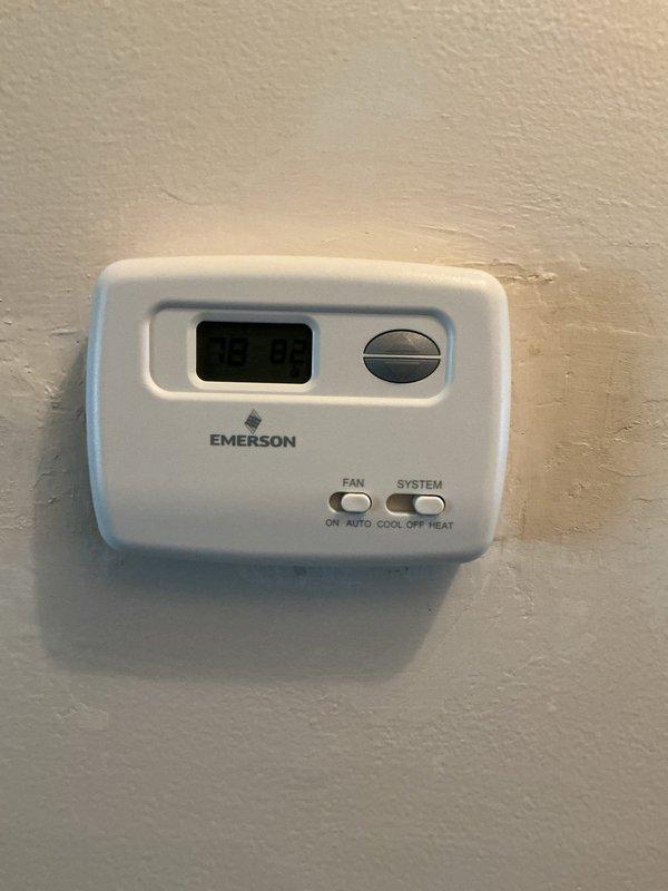 Responded to service call for thermostat malfunction and inconsistent heating. Upon arrival, inspected Emerson digital thermostat and removed cover to examine internal components. Found battery-powered unit with AAA batteries installed, circuit board, and wiring connections intact at terminal blocks. Verified thermostat display functionality showing temperature readings. Documented existing equipment condition with photographs of exterior unit and internal components including PCB, LCD display, battery compartment, and wire terminal connections for service records.