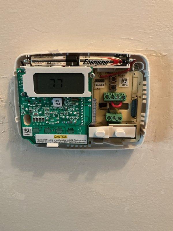 Responded to service call for thermostat malfunction and inconsistent heating. Upon arrival, inspected Emerson digital thermostat and removed cover to examine internal components. Found battery-powered unit with AAA batteries installed, circuit board, and wiring connections intact at terminal blocks. Verified thermostat display functionality showing temperature readings. Documented existing equipment condition with photographs of exterior unit and internal components including PCB, LCD display, battery compartment, and wire terminal connections for service records.
