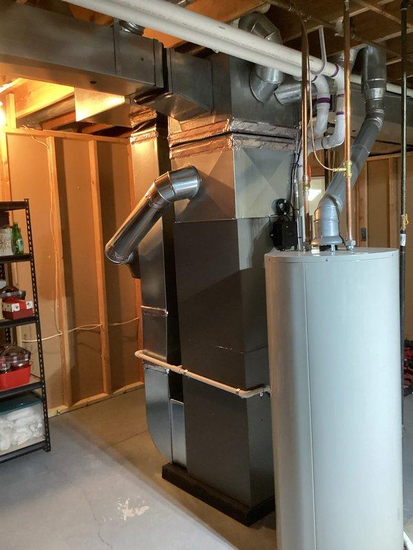 Completed full HVAC system installation in basement utility area including 90,000 BTU high-efficiency furnace with humidifier, 3-ton air conditioning unit with rear placement, and residential water heater. All ductwork, ventilation piping, and electrical connections were installed per code specifications. PVC condensate and exhaust venting routed through ceiling joists with proper pitch and support. Sheet metal supply and return ductwork fabricated and connected to furnace plenum. Flexible duct transitions installed where required for equipment connections. Water heater positioned adjacent to furnace with appropriate clearances for service access. All gas piping, water lines, and drain connections completed and tested for leaks. Air conditioning refrigerant lines run to outdoor condenser unit and system charged to manufacturer specifications. Thermostat wiring pulled and connected to new furnace control board. Humidifier integrated into supply plenum with water line and drain installed