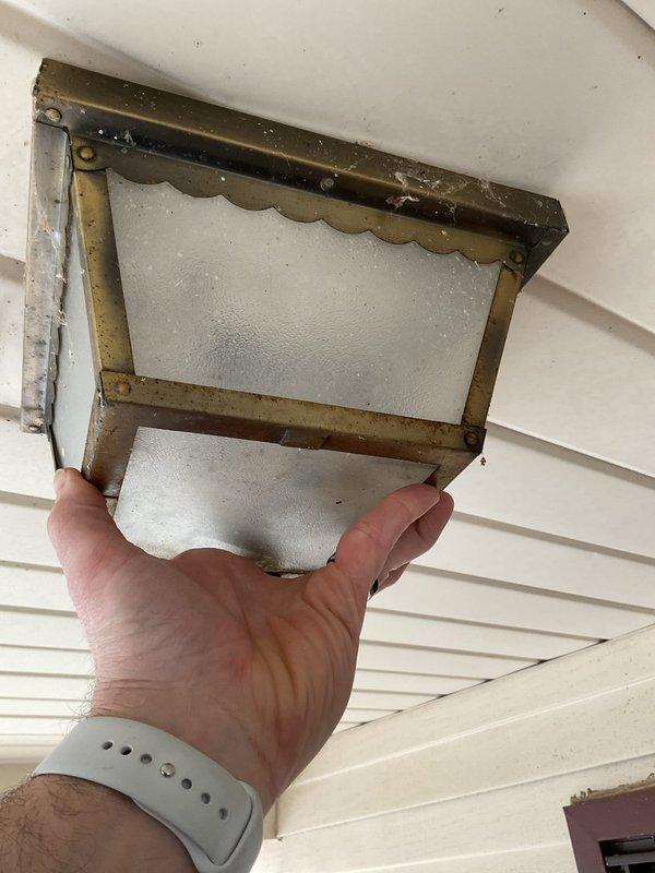 Replaced deteriorated outdoor porch light fixture with new flush-mount ceiling fixture featuring bronze finish and textured glass shade. Removed heavily corroded wall-mounted fixture showing significant weather damage and rust accumulation, disconnected existing wiring, and installed updated fixture to ceiling mount position for improved aesthetics and functionality. Additionally, repaired ceiling fan pull chain mechanism that had been improperly installed during previous replacement attempt, restoring full operational control to the fan unit.