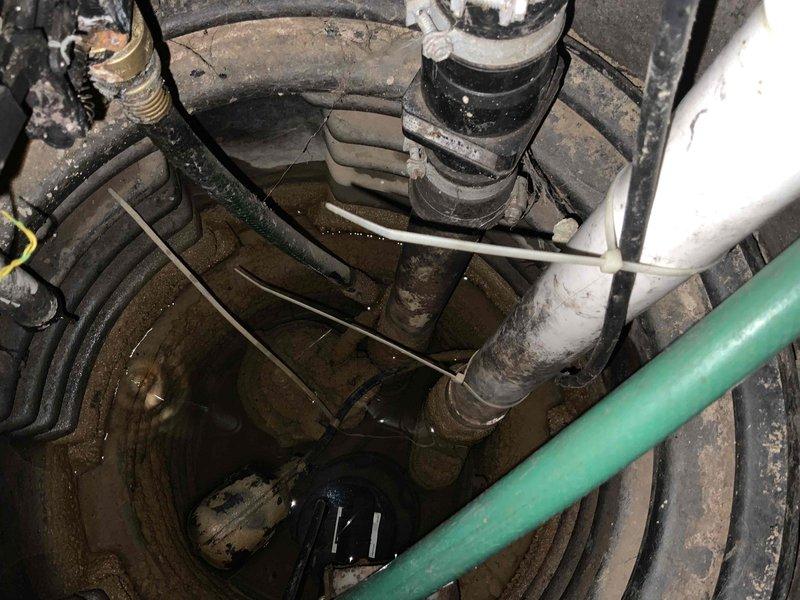 Completed assessment and estimate for sump pump replacement in 43-year-old residential property. Inspected existing submersible sump pump system with floating switch mechanism located in circular ridged plastic basin. Documented deteriorating conditions including standing water accumulation, aged plumbing connections with multiple PVC and flexible drainage lines, and pump equipment showing signs of extended service life. Photographed entire sump pit assembly, discharge piping configuration, electrical wiring routing, and surrounding basement infrastructure to provide comprehensive documentation for replacement proposal.