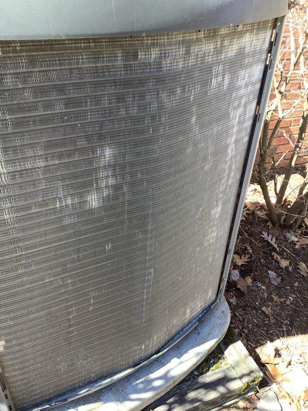 Completed annual preventive maintenance on Lennox air conditioning condensing unit. Inspected condenser coil and found moderate dirt and debris accumulation on exterior fins. Cleared leaves and debris from around unit base and perimeter. Evaluated protective grille screens for proper airflow and noted environmental buildup consistent with outdoor exposure. Verified condenser coil fins remain intact with proper spacing throughout. Unit operational and positioned on stable concrete pad against brick wall exterior. All components accessible for routine maintenance procedures.