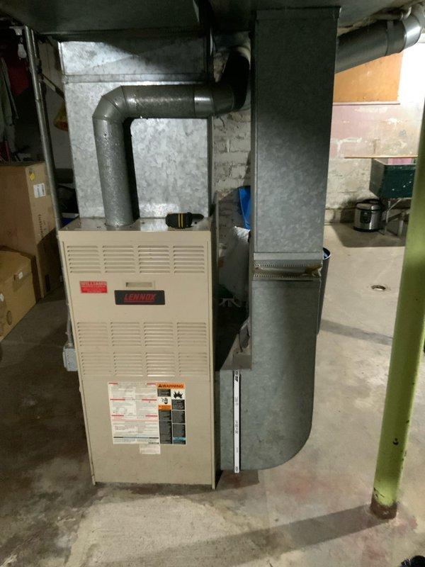Conducted comprehensive assessment of 32-year-old residential furnace system for replacement estimate. Documented existing HVAC equipment configuration including furnace unit, ductwork connections, and electrical service panel in basement utility area. Photographed current system installation, noting beige cabinet-style furnace with digital display, gray ductwork routing, electrical panel with fuse holders, and overall mechanical room layout to provide accurate replacement specifications and equipment sizing recommendations.