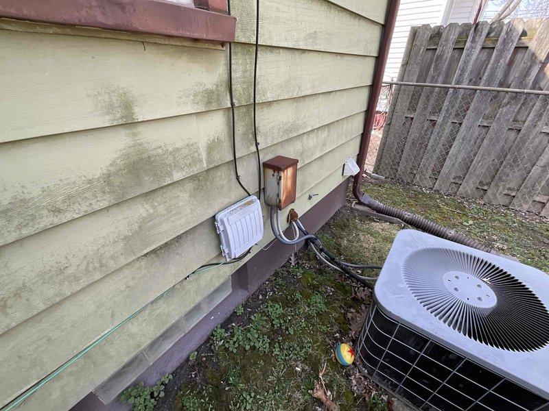 Conducted on-site assessment for central air conditioning system replacement at residential property. Inspected existing outdoor condensing unit, refrigerant line set, electrical disconnect, and associated components along exterior wall. Documented current system configuration including condenser placement, electrical service panel with circuit breakers, and refrigerant piping routing. Evaluated installation area conditions, noting exterior siding condition and ground surface characteristics that may impact replacement installation. Photographed existing equipment and electrical infrastructure to support replacement system specifications and quote preparation.