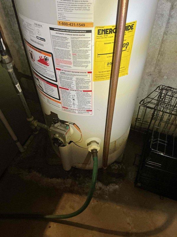 Assessed existing natural draft water heater in residential basement utility room for replacement quote. Unit currently operational with standard tank configuration, copper supply lines, and gas connections visible at base. Documented existing installation including venting system with galvanized ductwork and elbow joints, though complete venting photography was limited due to access constraints in confined space.