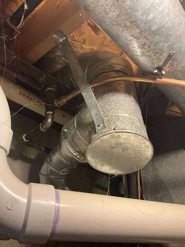 Assessed existing natural draft water heater in residential basement utility room for replacement quote. Unit currently operational with standard tank configuration, copper supply lines, and gas connections visible at base. Documented existing installation including venting system with galvanized ductwork and elbow joints, though complete venting photography was limited due to access constraints in confined space.