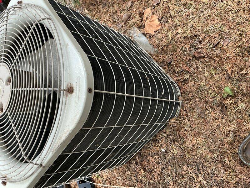 Completed annual preventive maintenance on outdoor cylindrical condenser unit. Inspected fan assembly, verified fan blade operation through protective grille, and examined heat exchanger coils for damage or deterioration. Cleaned debris from surrounding area including pine needles and leaf litter. Verified protective wire guard integrity and checked all mounting hardware and fasteners for security. Unit operational with no immediate repairs required.