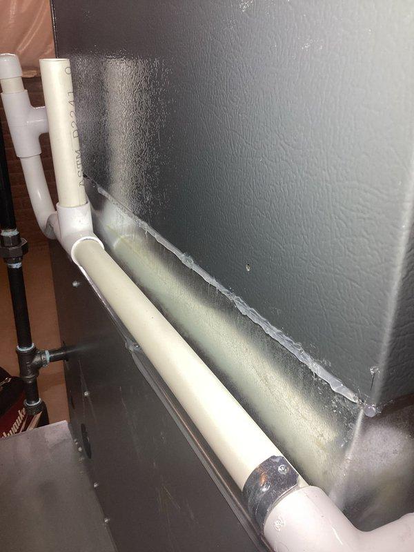 Responded to service call for loud humming/buzzing noise from 2-year-old furnace system located in basement. Upon inspection, discovered significant condensation and moisture accumulation on air handler cabinet and supply plenum, with water droplets and streaking visible on metal surfaces. Identified excessive condensation issue likely caused by inadequate insulation or air leakage creating temperature differential between conditioned air and ambient conditions. Examined condensate drain system including white PVC drainage lines and connections. Documented moisture patterns on equipment surfaces and assessed potential impact on system operation and noise complaint. Verified condensate drain line routing and functionality. Equipment remains under parts and labor warranty coverage.