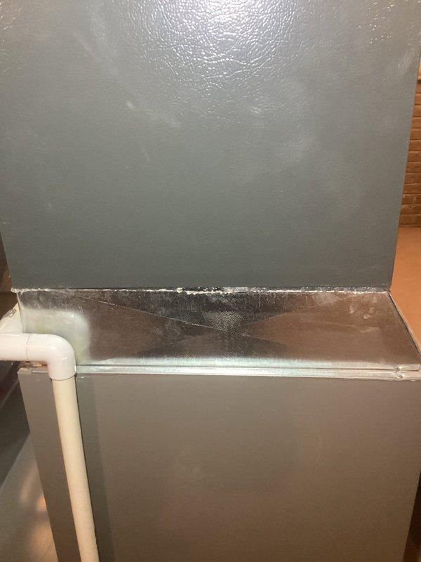 Responded to service call for loud humming/buzzing noise from 2-year-old furnace system located in basement. Upon inspection, discovered significant condensation and moisture accumulation on air handler cabinet and supply plenum, with water droplets and streaking visible on metal surfaces. Identified excessive condensation issue likely caused by inadequate insulation or air leakage creating temperature differential between conditioned air and ambient conditions. Examined condensate drain system including white PVC drainage lines and connections. Documented moisture patterns on equipment surfaces and assessed potential impact on system operation and noise complaint. Verified condensate drain line routing and functionality. Equipment remains under parts and labor warranty coverage.