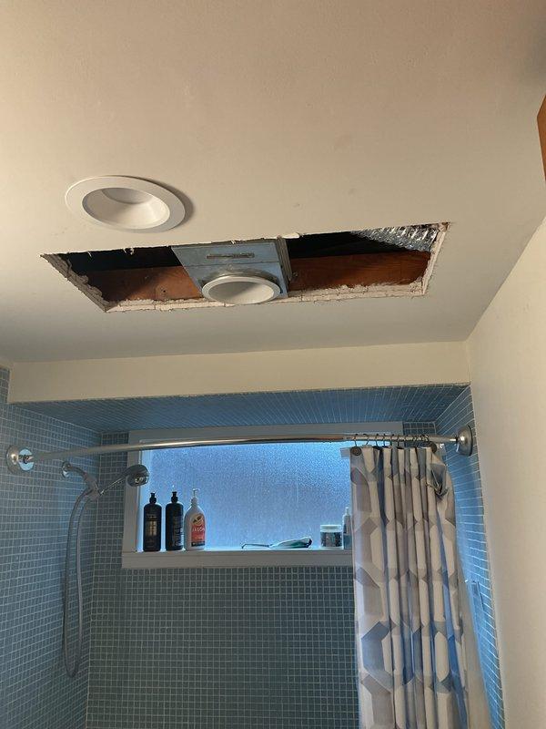 Completed electrical installation work in bathroom, including installation of recessed lighting fixture and ventilation fan with grille in ceiling above tiled shower area. Work required access through ceiling opening to properly wire and secure fixtures to wooden joists, with all electrical connections made per code and permits obtained prior to installation.