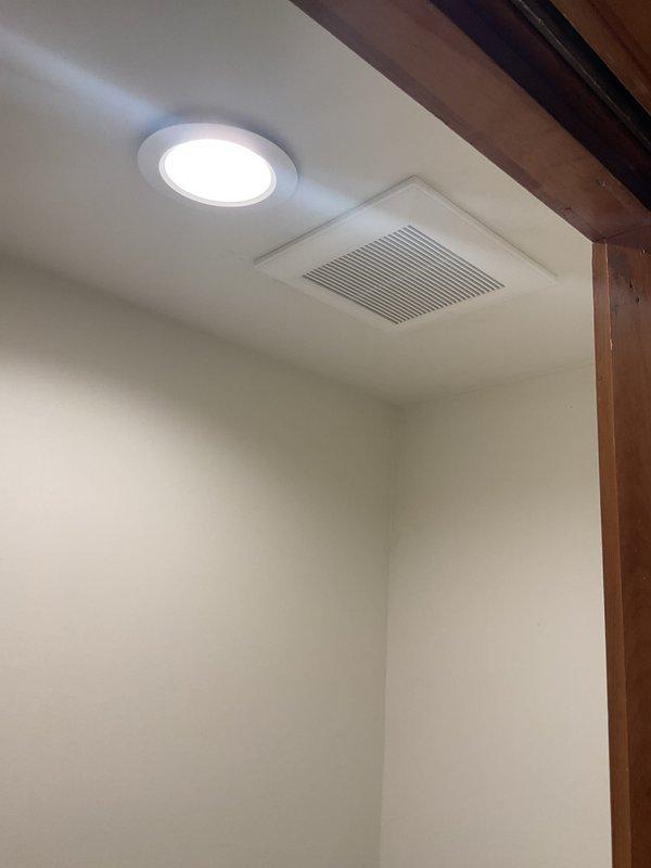 Completed electrical installation work in bathroom, including installation of recessed lighting fixture and ventilation fan with grille in ceiling above tiled shower area. Work required access through ceiling opening to properly wire and secure fixtures to wooden joists, with all electrical connections made per code and permits obtained prior to installation.