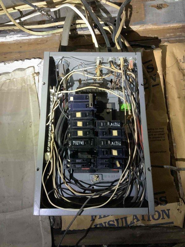 Conducted comprehensive electrical panel upgrade estimate in unfinished basement area. Assessed existing gray metal circuit breaker panel with dual-row breaker configuration, evaluating current wiring conditions including mixed conductor types entering from top and bottom of enclosure. Documented panel location in corner area with exposed ceiling joists and identified accessibility considerations including basement moisture conditions evidenced by wall staining and deterioration on cinder block surfaces. Photographed existing electrical infrastructure, noting wire routing through wooden framing members and current breaker arrangement with indicator markings. Evaluated surrounding environment including proximity to insulation materials and freezer appliance to determine clearance requirements for potential panel replacement or upgrade work.