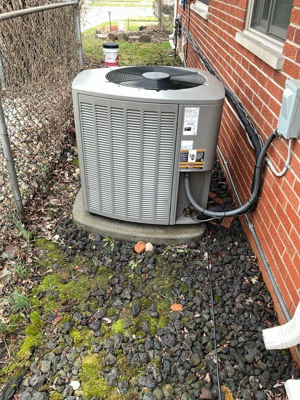 Performed comprehensive air conditioning maintenance on residential outdoor condenser unit. Conducted visual inspection of unit exterior, verifying proper placement on concrete pad and checking for physical damage or deterioration. Inspected electrical conduit connections and verified secure attachment to building structure. 

Removed debris, leaves, and organic material from surrounding gravel base and unit perimeter to ensure adequate airflow and drainage. Noted moss growth in gravel bed indicating moisture retention in area. Checked manufacturer labels and unit specifications for proper identification and maintenance requirements.

Assessed top-mounted fan assembly and protective grille for structural integrity and proper operation. Utilized diagnostic gauges to measure system pressures and verify refrigerant charge levels. Inspected condenser coil fins through louver openings for blockage, damage, or excessive dirt accumulation. Verified unit levelness on pad and checked for signs 